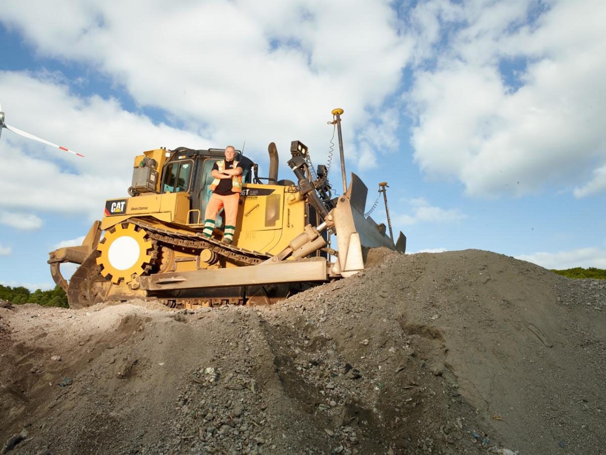 Mitarbeiter vor Arbeitsmaschine auf Materialaufschüttung